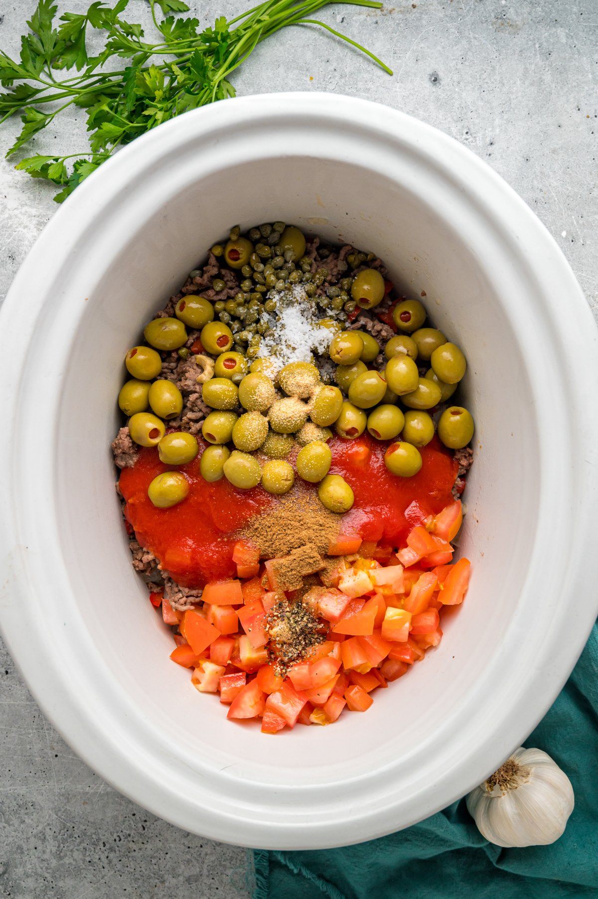 Picadillo ingredients added to cooked ground beef in a crockpot.