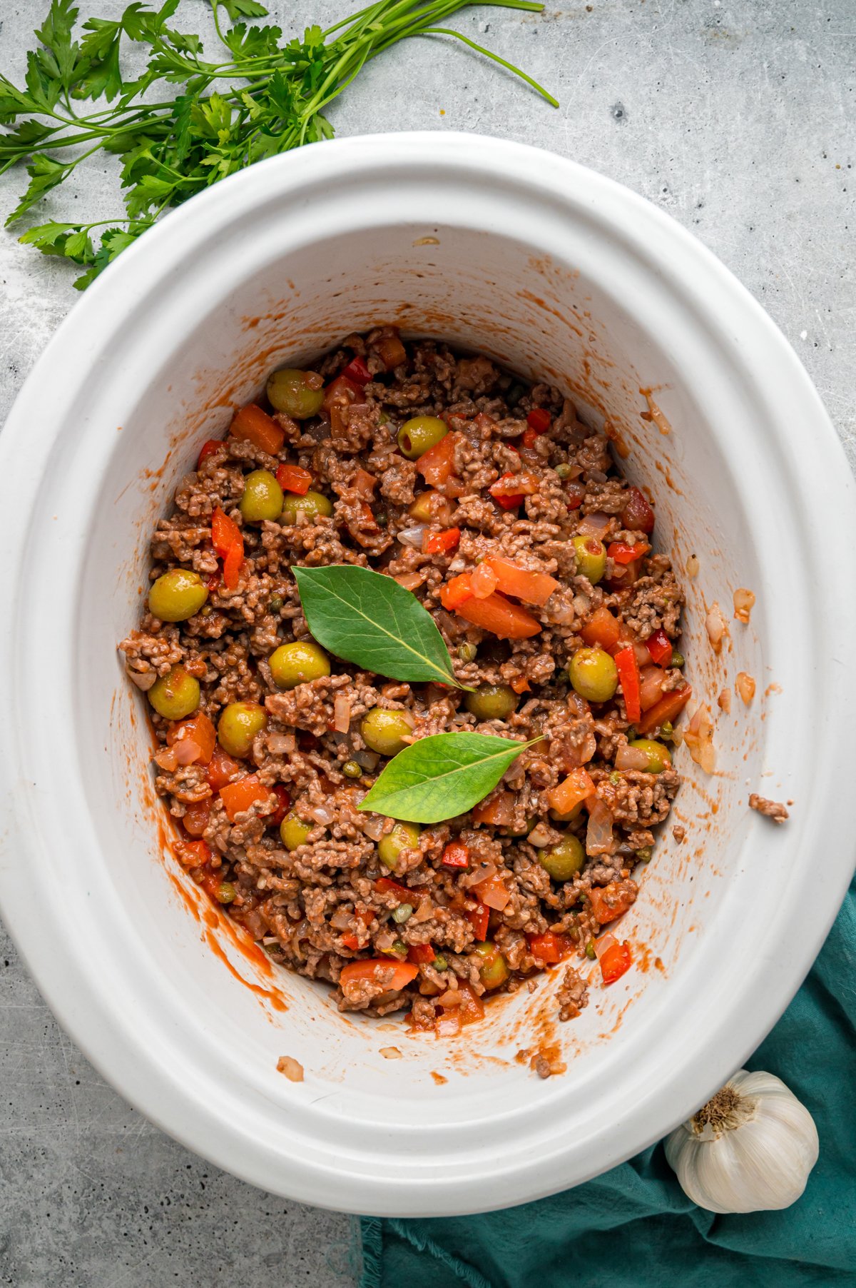 Bay leaves added to stirred picadillo mixture in a crockpot.