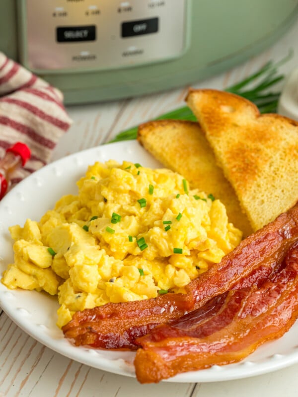 Slow cooker scrambled eggs on a plate with bacon and toast.