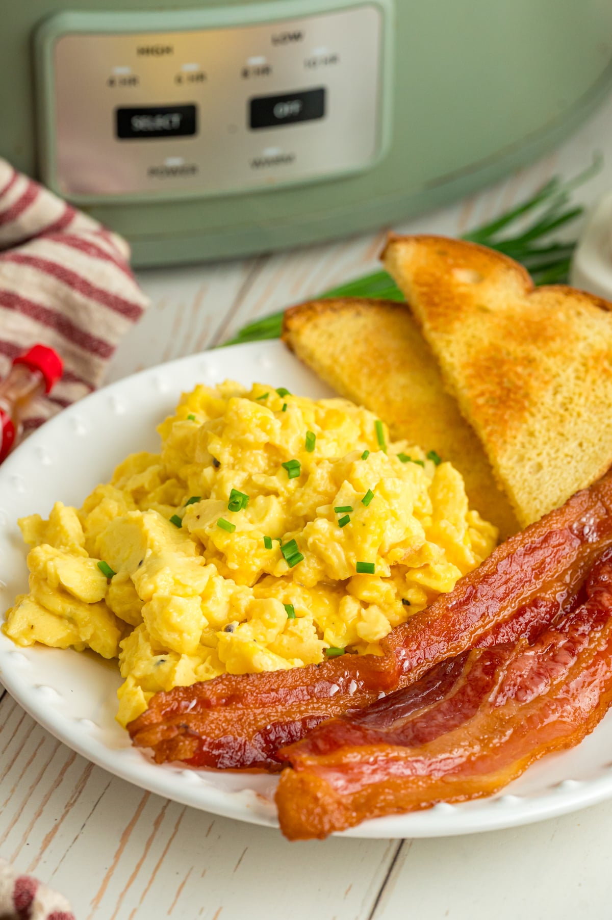 Slow cooker scrambled eggs on a plate with bacon and toast.