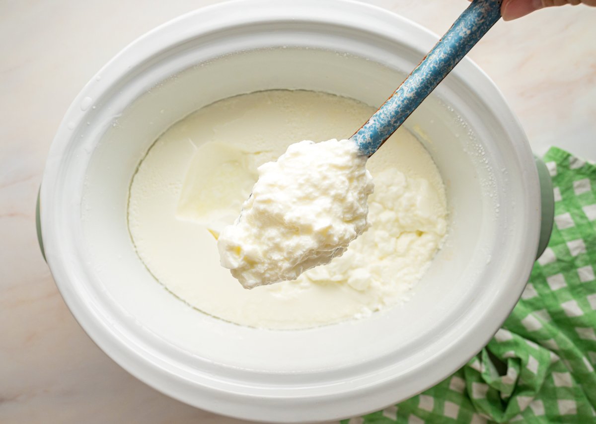 Scooping some yogurt from a slow cooker with a spoon.