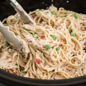Tongs grabbing some slow cooker chicken carbonara from a crockpot.