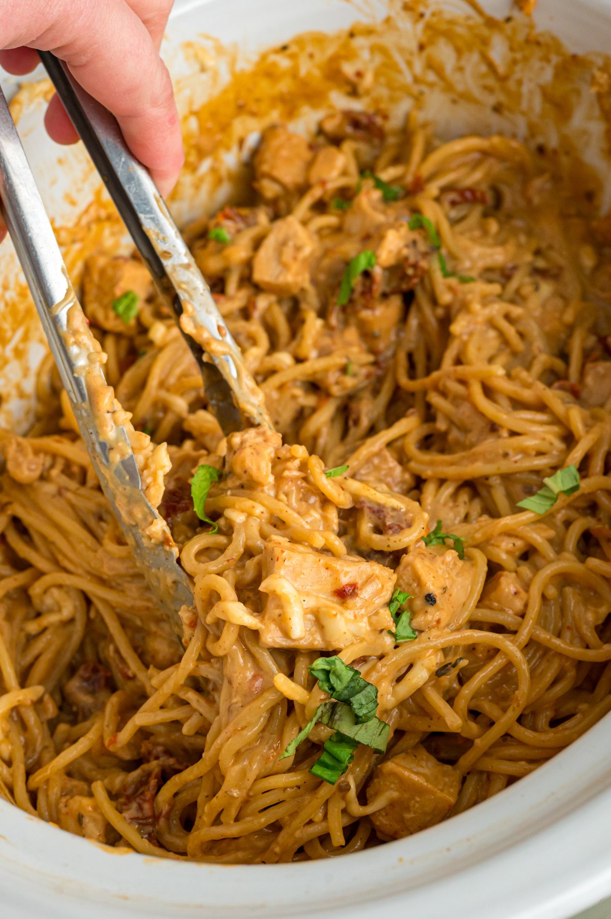 A hand holding tongs grabbing some slow cooker marry me chicken pasta.