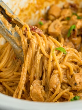 Tongs grabbing slow cooker marry me chicken from a crockpot.