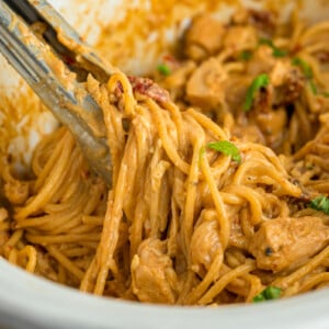 Tongs grabbing slow cooker marry me chicken from a crockpot.