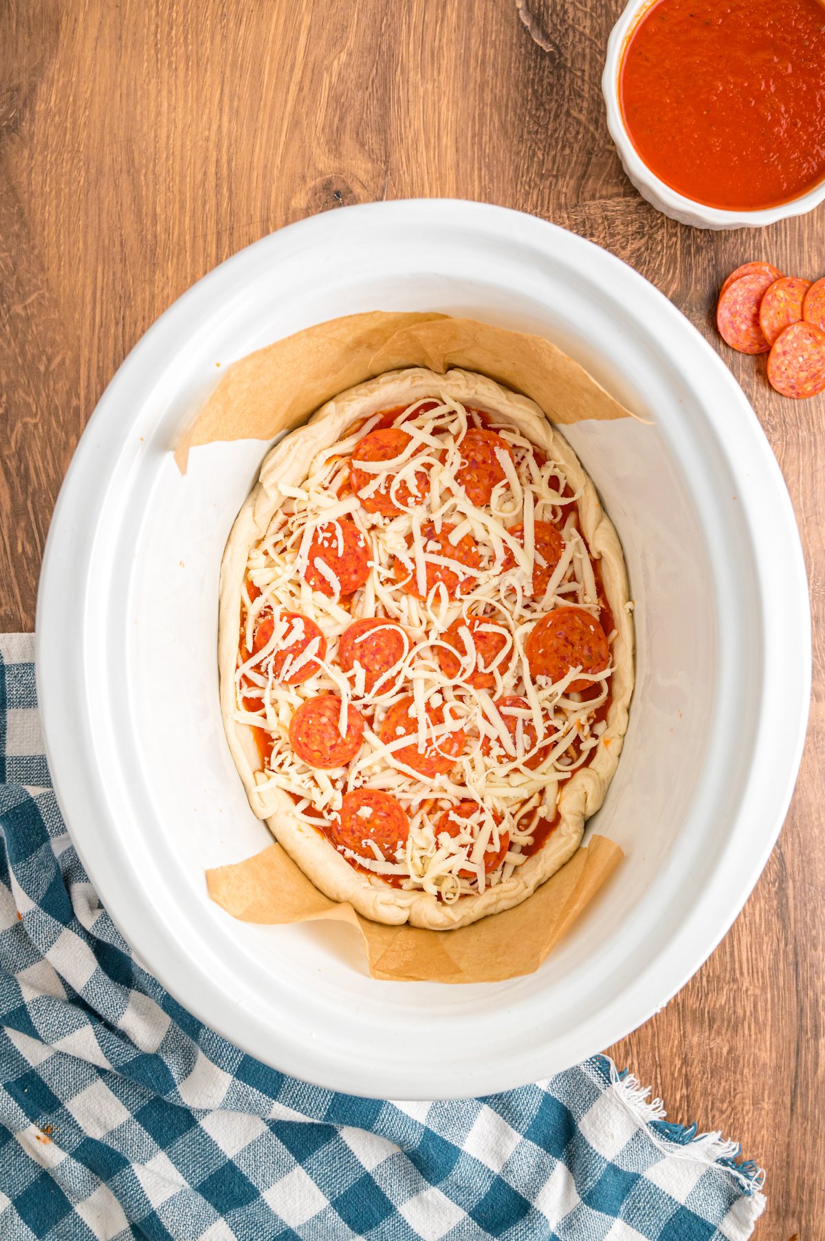 Cheese and pepperoni on top of pizza dough and sauce in a slow cooker.