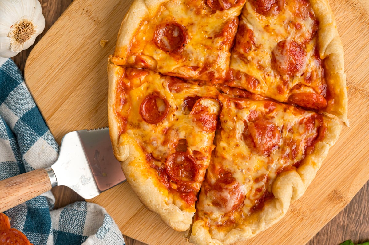Slow cooker pizza cut into four slices on a wooden board.