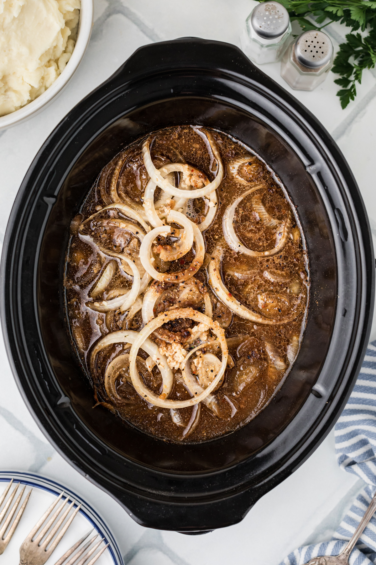 Gravy mixture added to steak and onions in a crockpot.