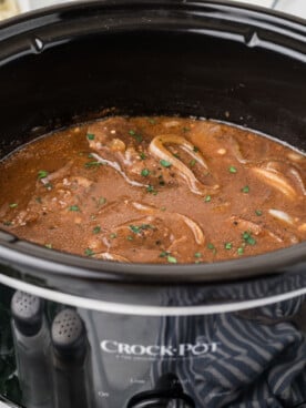 Steak and onions in a black crockpot.