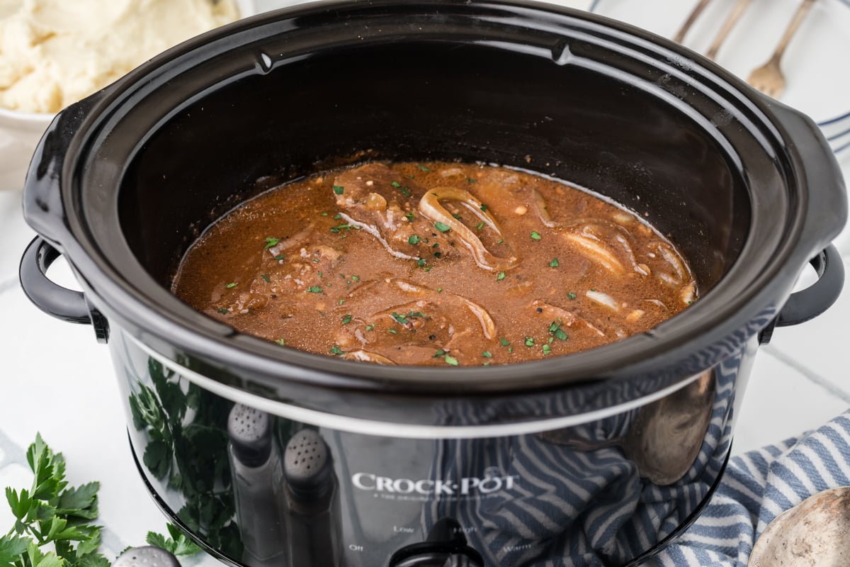 Steak and onions in a black crockpot.