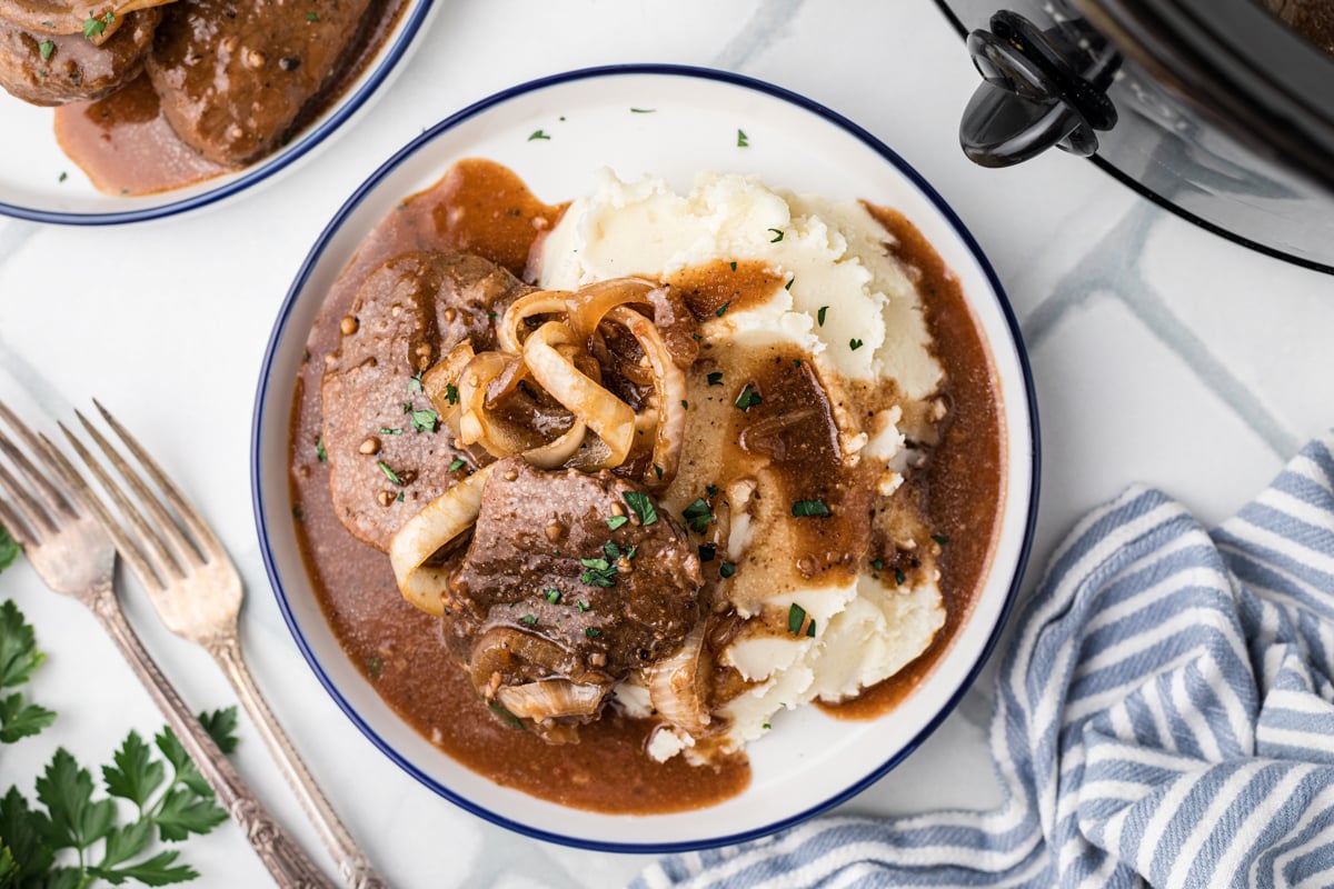 A bowl with steak and onions and mashed potatoes.
