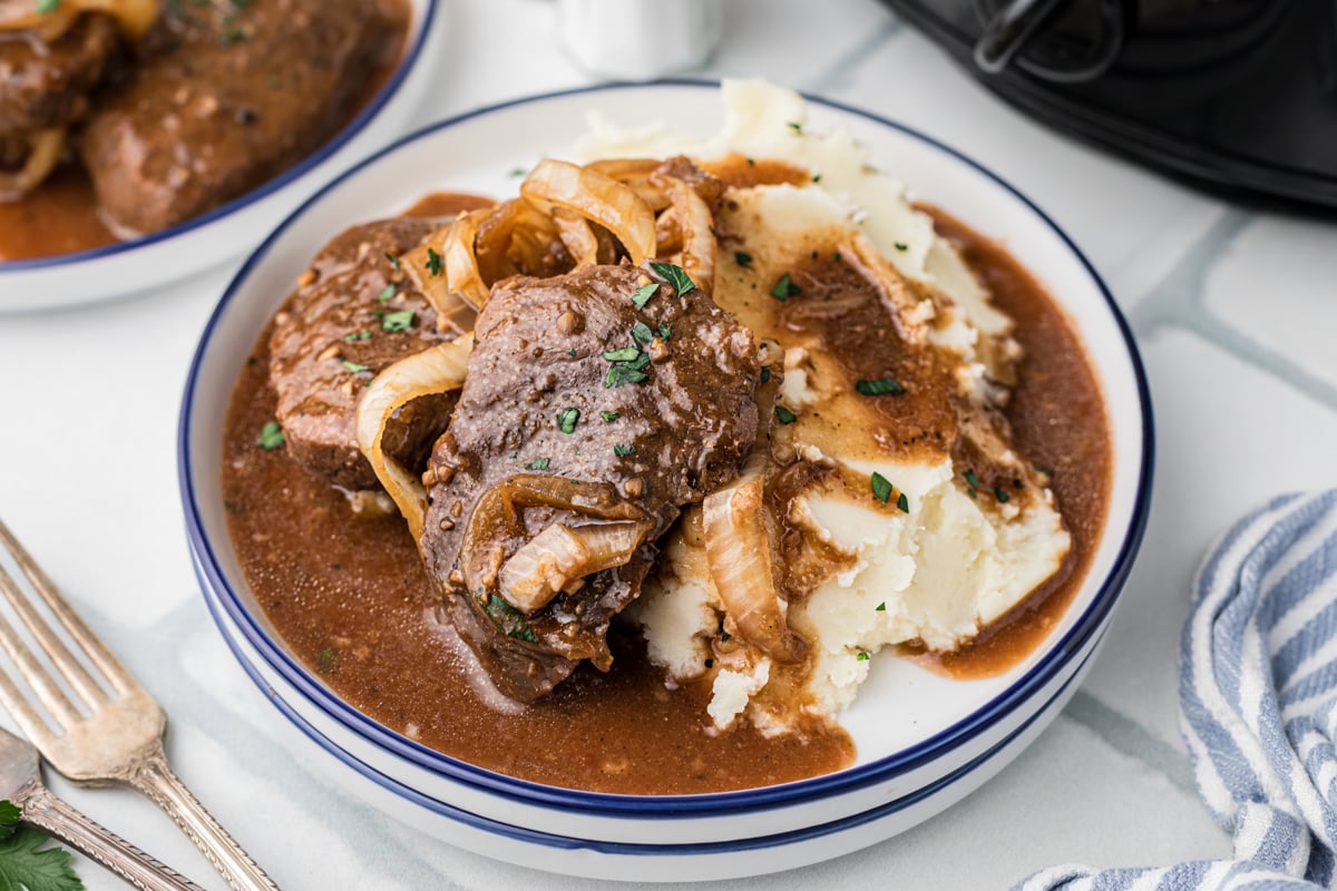 A serving of steak and onions with mashed potatoes in a bowl.