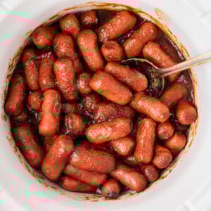 Slow cooker apple butter little smokies with a spoon.