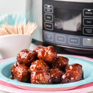Slow cooker baby shower meatballs on a stack of pink and blue plates.