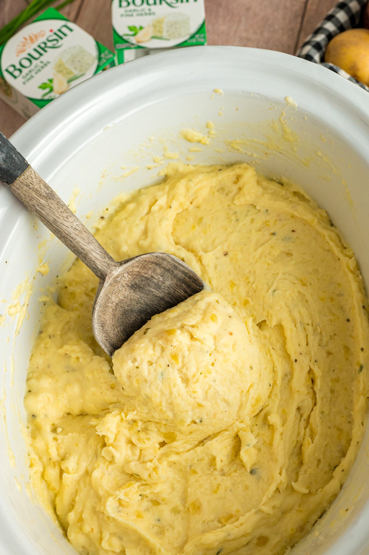Slow cooker boursin cheese potatoes with a wooden spoon scooping some out.