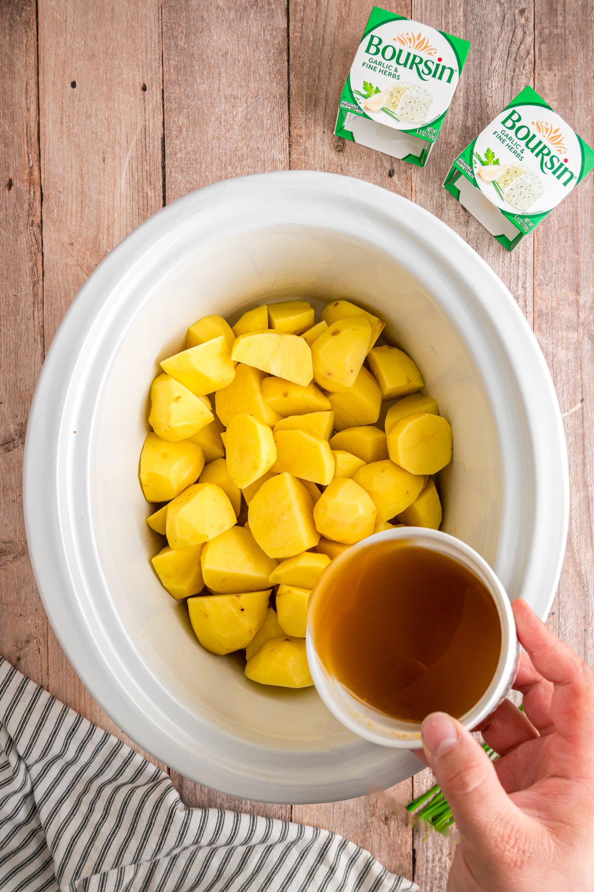 Pouring broth into a crockpot with potatoes in it.