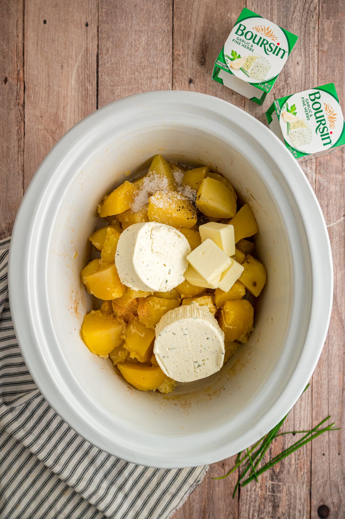 Boursin cheese, butter, and seasonings added to potatoes in a crockpot.