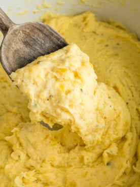 A wooden spoon with a scoop of slow cooker boursin cheese potatoes.