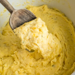 A wooden spoon with a scoop of slow cooker boursin cheese potatoes.