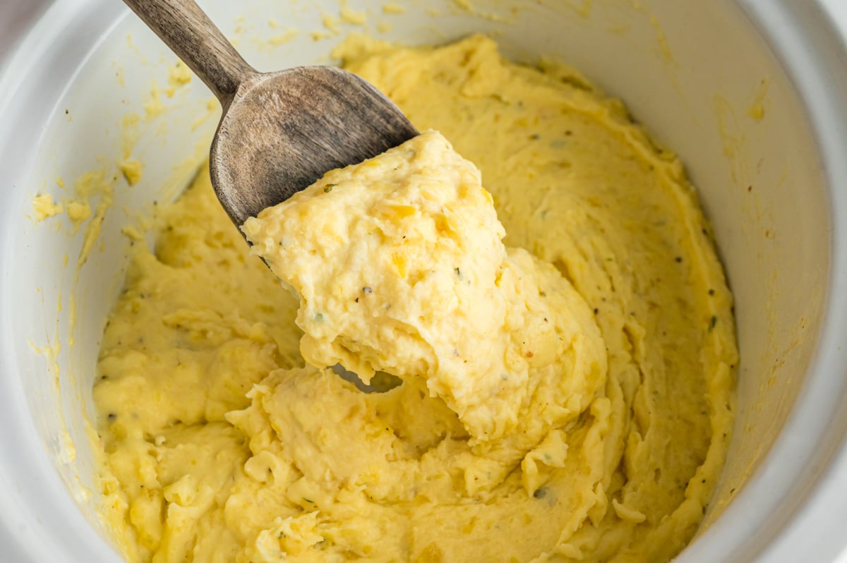 A wooden spoon with a scoop of slow cooker boursin cheese potatoes.