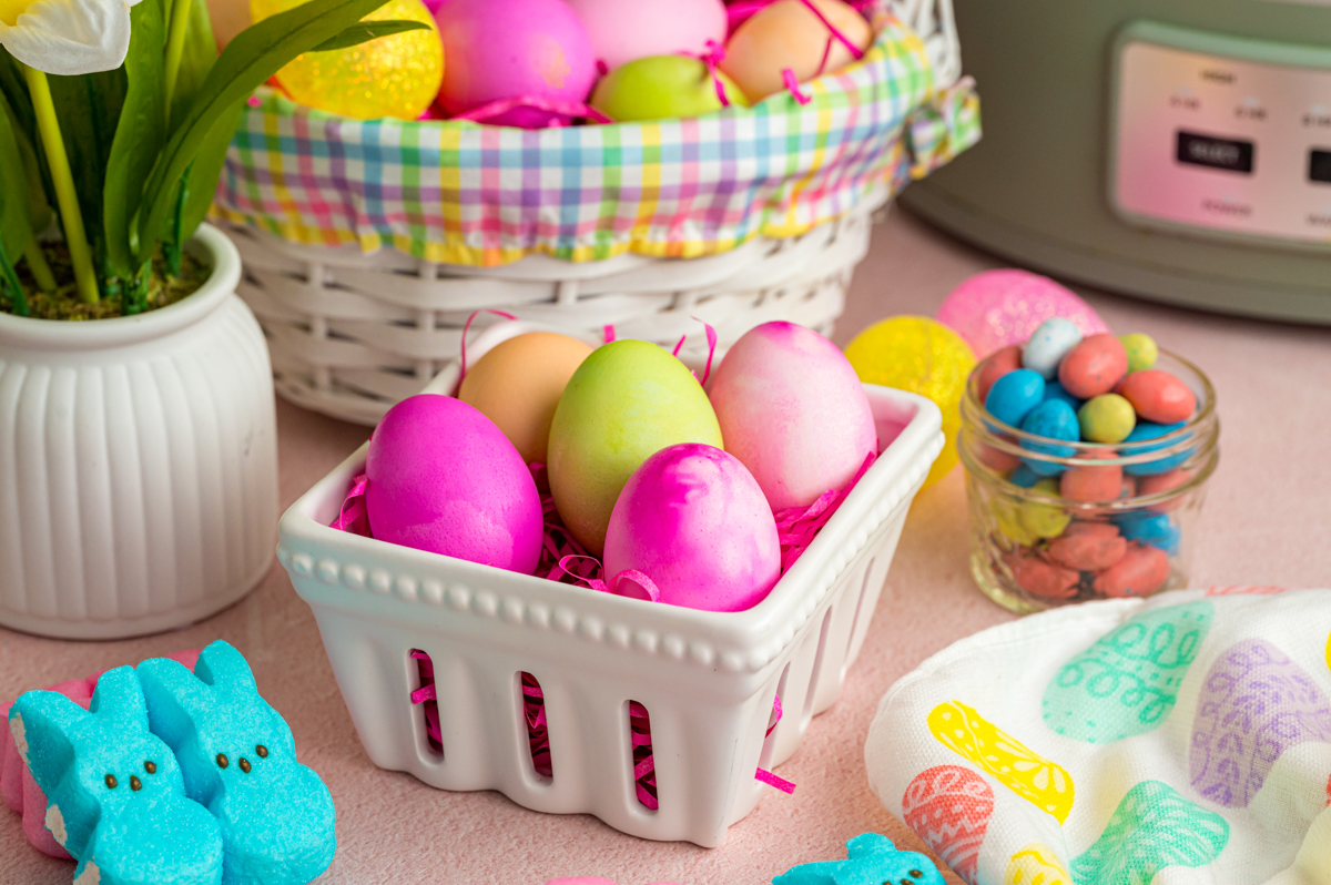 Slow cooker easter eggs in  a small white basket with more in the background.