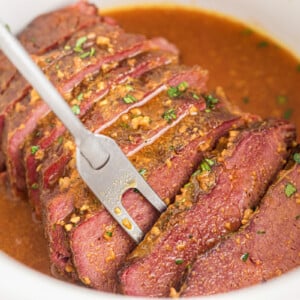 Slow cooker maple mustard corned beef with a serving fork taking a piece.