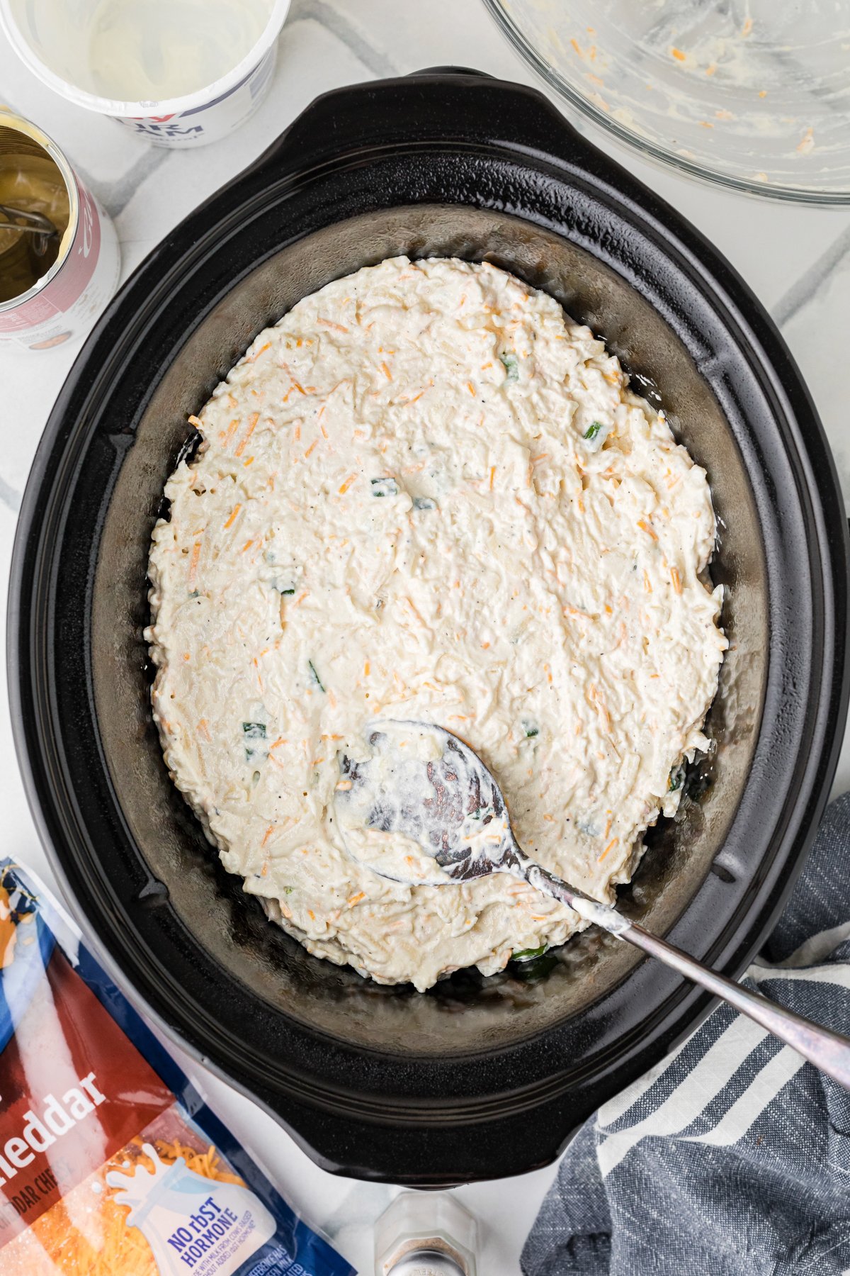 Party potatoes mixture in a crockpot with a spoon.