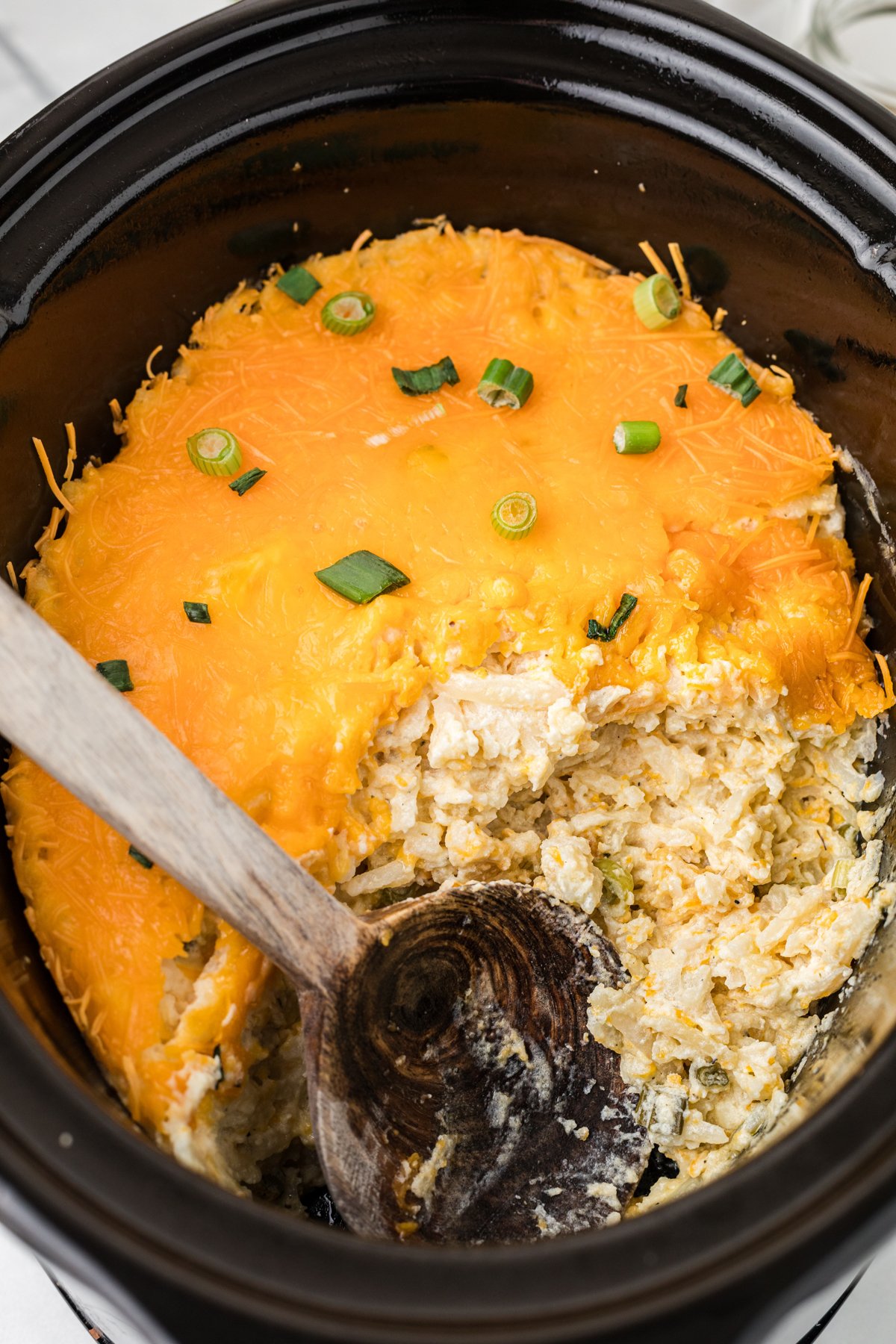Slow cooker party potatoes with a large wooden spoon in the crockpot.