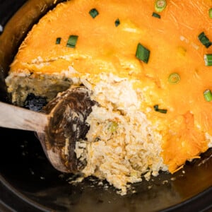 A large wooden spoon scooping out some slow cooker party potatoes.