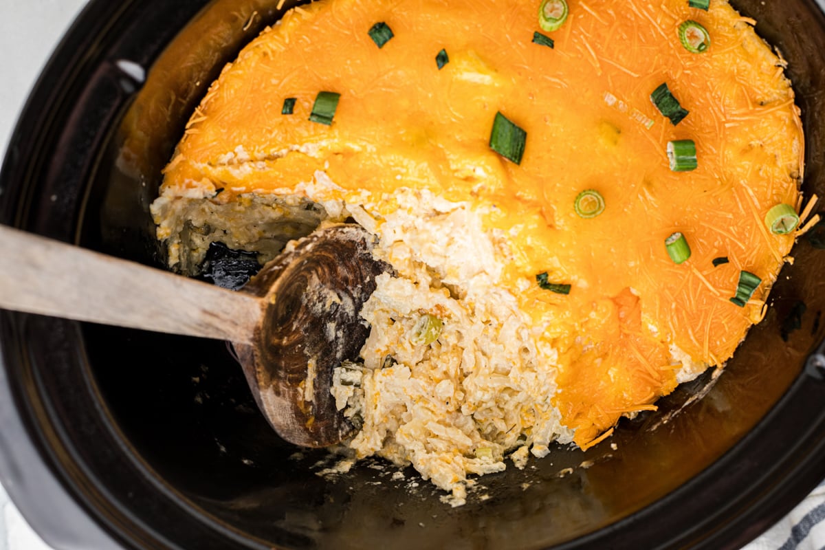 A large wooden spoon scooping out some slow cooker party potatoes.
