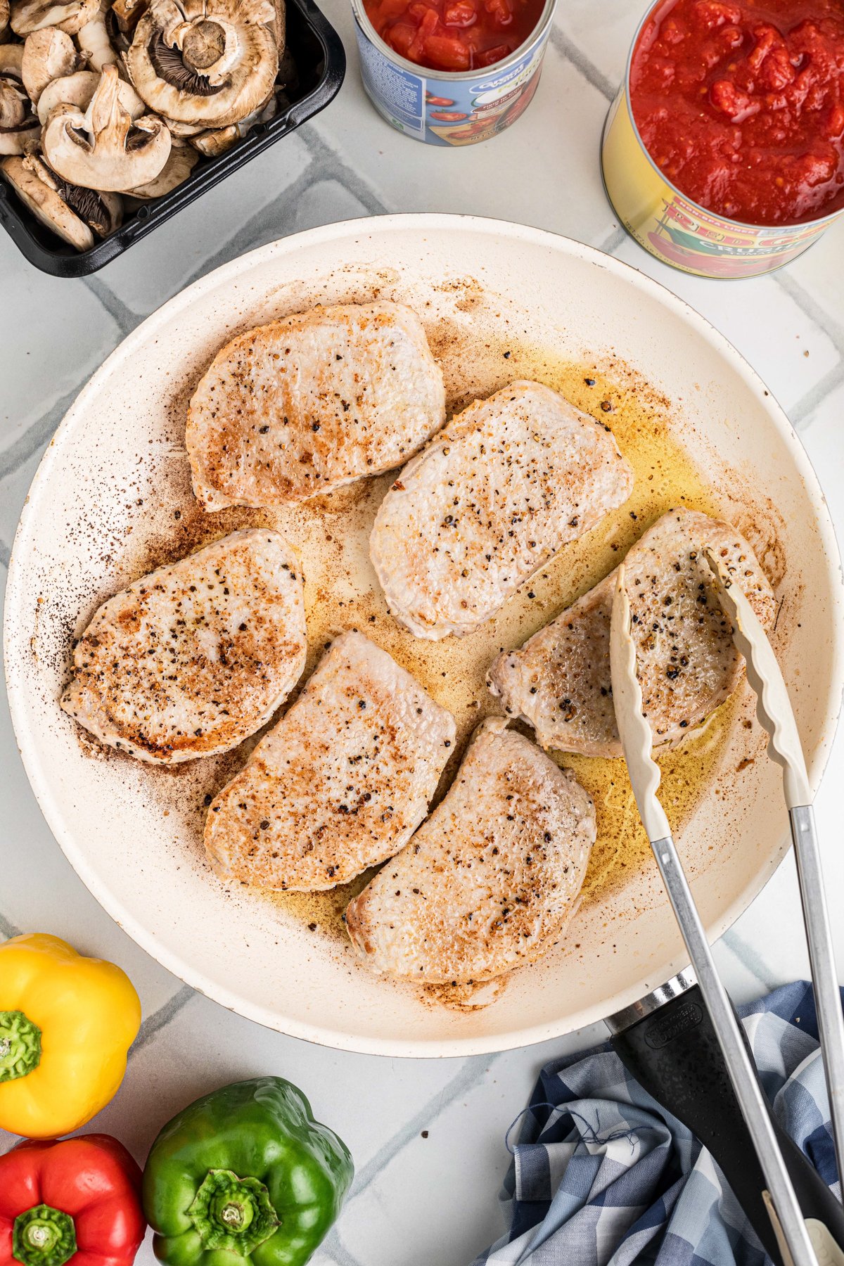 Pork chops being seared in a skillet with olive oil.