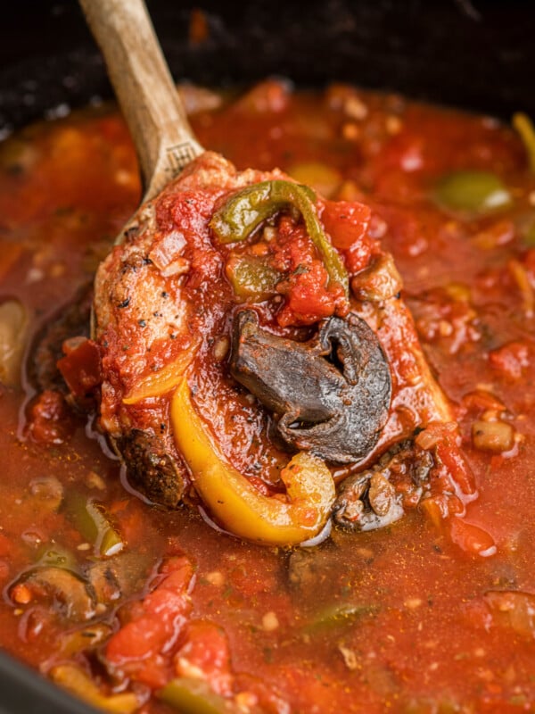 Slow cooker pork chop cacciatore with a wooden spoon scooping some out.