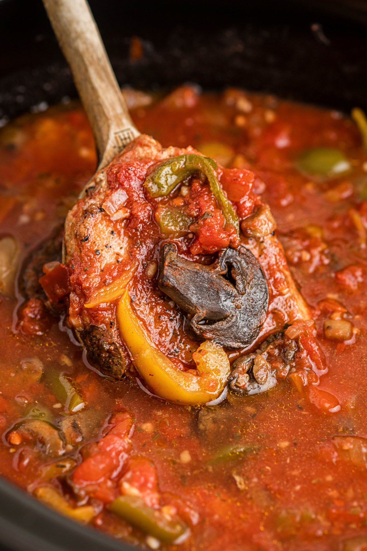 Slow cooker pork chop cacciatore with a wooden spoon scooping some out.