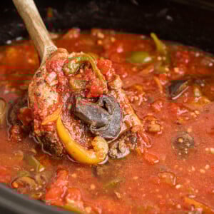 A wooden spoon scooping out slow cooker pork chop cacciatore.