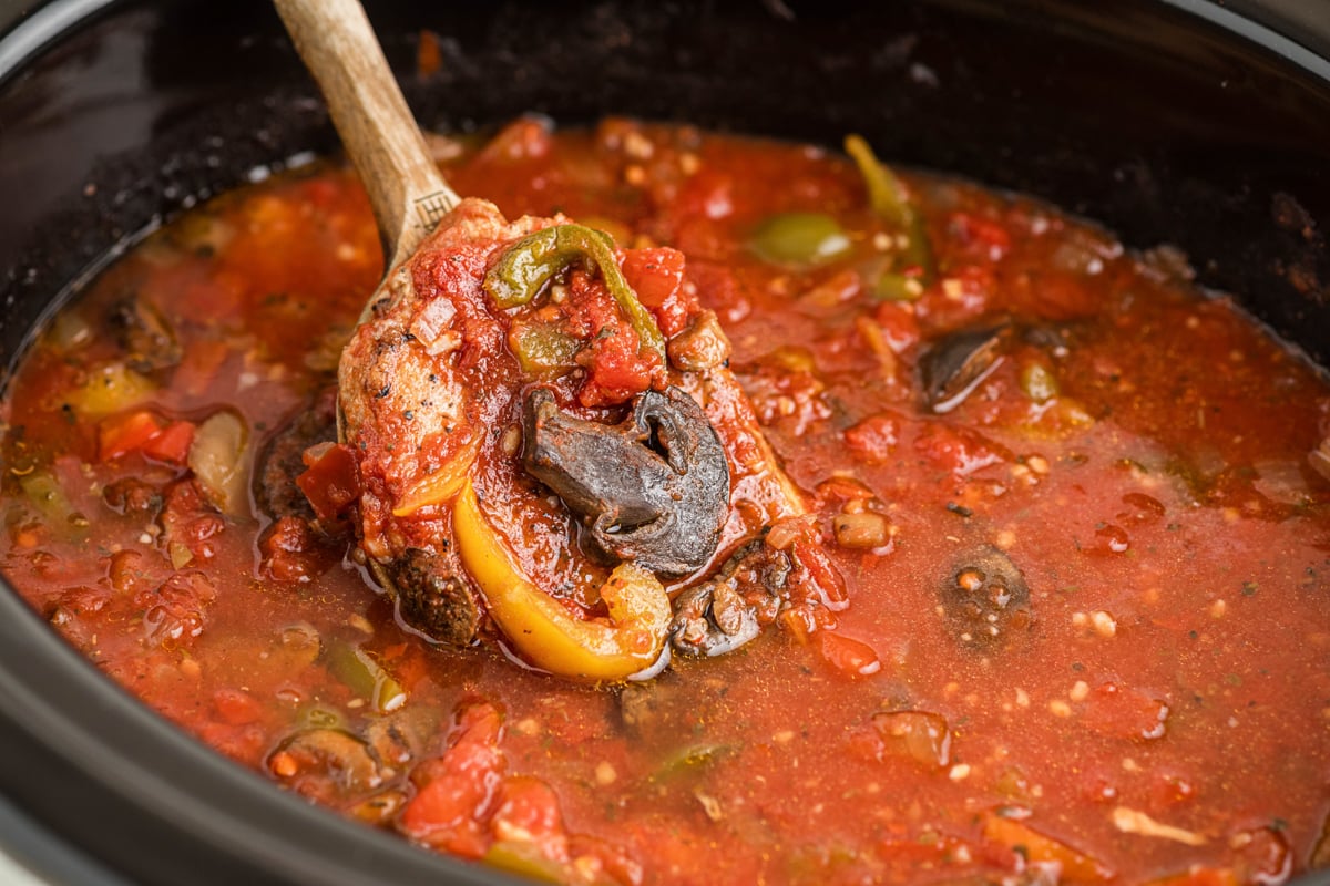 A wooden spoon scooping out slow cooker pork chop cacciatore.