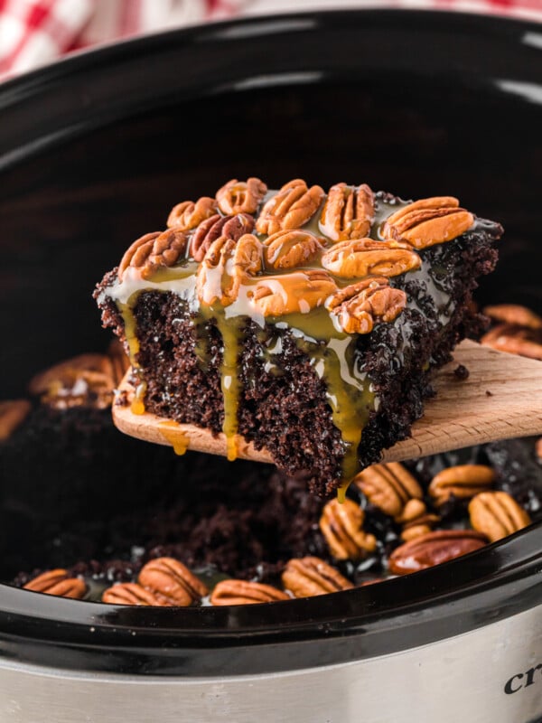 A slice of slow cooker turtle cake being held up on a wooden spatula.