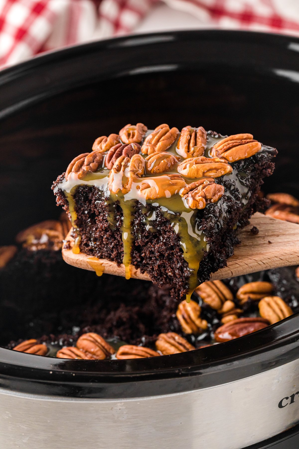 A slice of slow cooker turtle cake being held up on a wooden spatula.