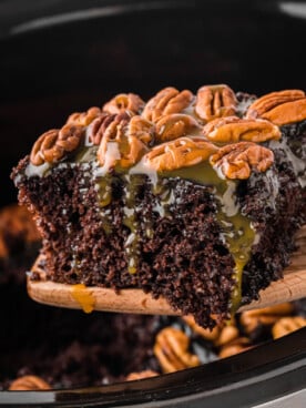 A wooden spatula holding up a slice of slow cooker turtle cake.