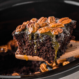 A wooden spatula holding up a slice of slow cooker turtle cake.