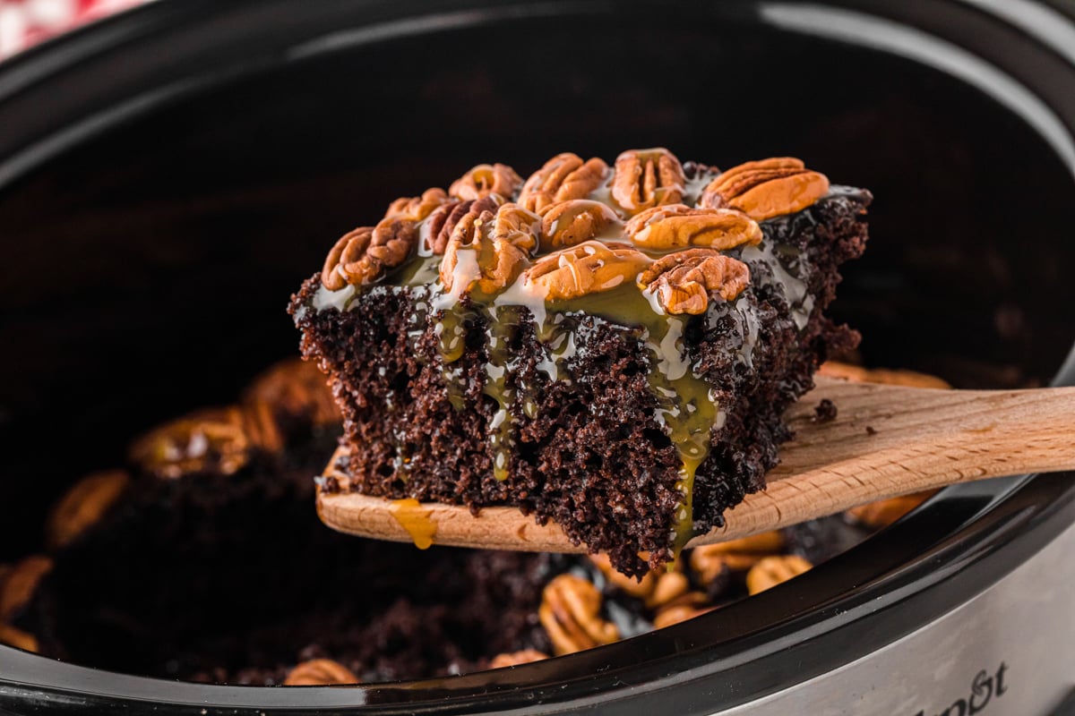 A wooden spatula holding up a slice of slow cooker turtle cake.