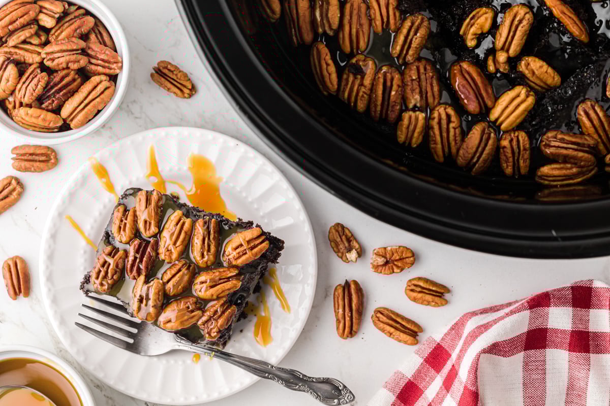 A slice of slow cooker turtle cake on a plate next to a crockpot.
