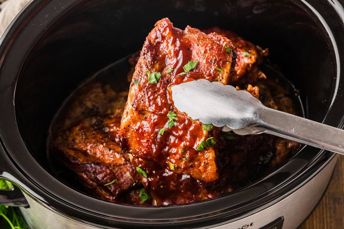 Tongs holding up a section of slow cooker baby back ribs.