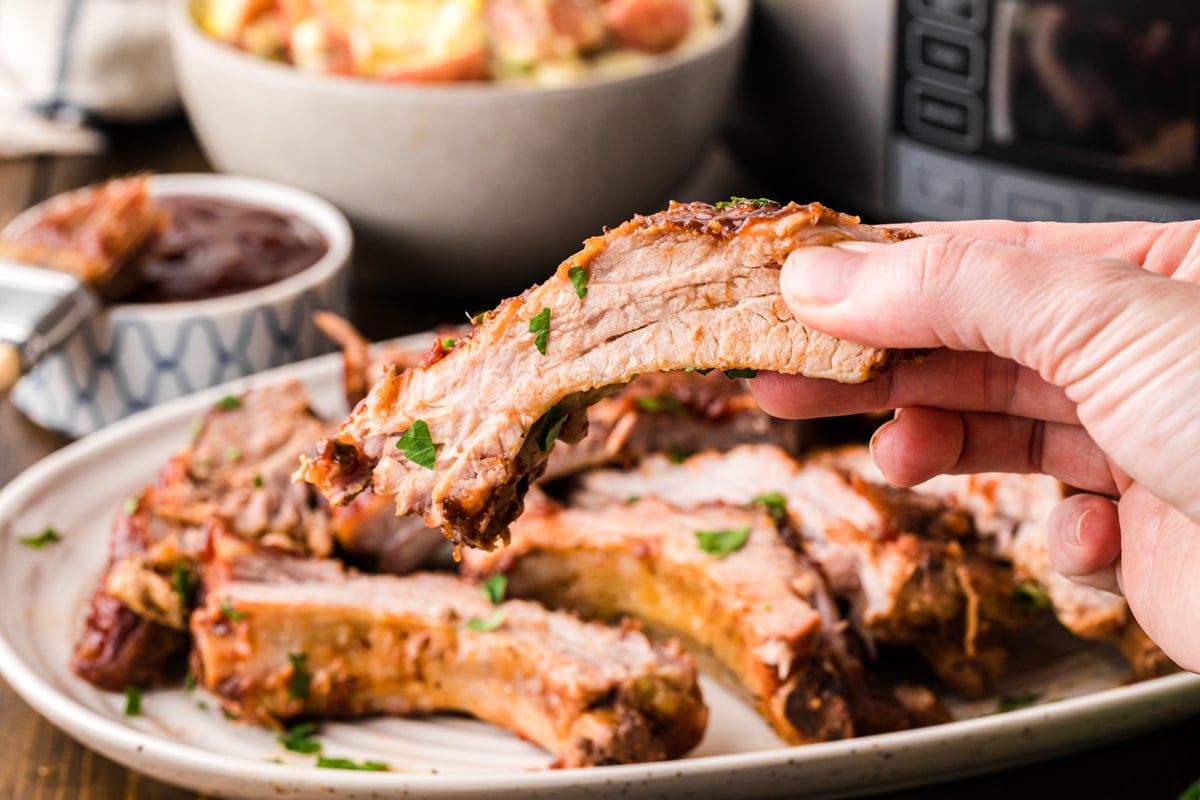 A hand holding up one of the slow cooker baby back ribs.