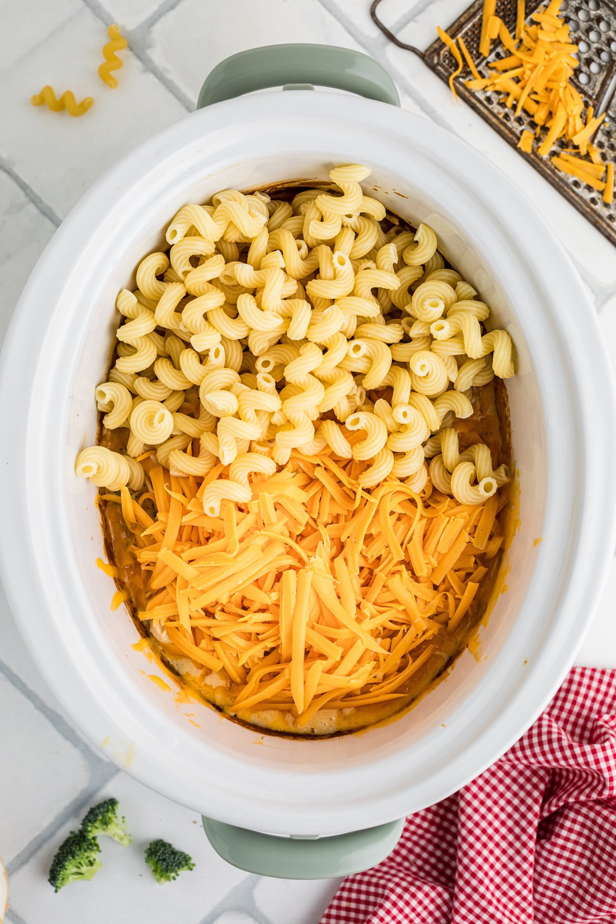 Pasta noodles and cheddar cheese added to ingredients in a slow cooker.