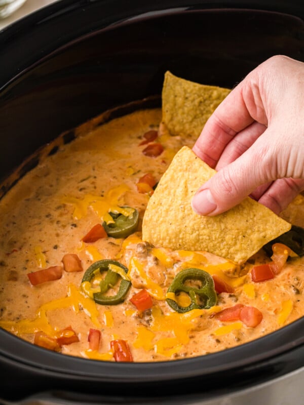 A hand dipping a tortilla chip into slow cooker taco dip.