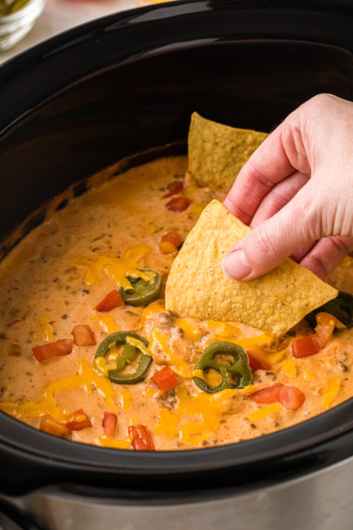 A hand dipping a tortilla chip into slow cooker taco dip.