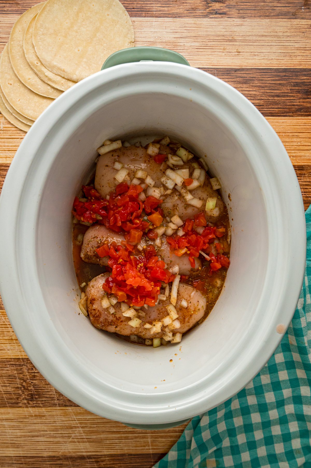 Chicken breasts, seasonings, rotel, broth, and onions in a crockpot.