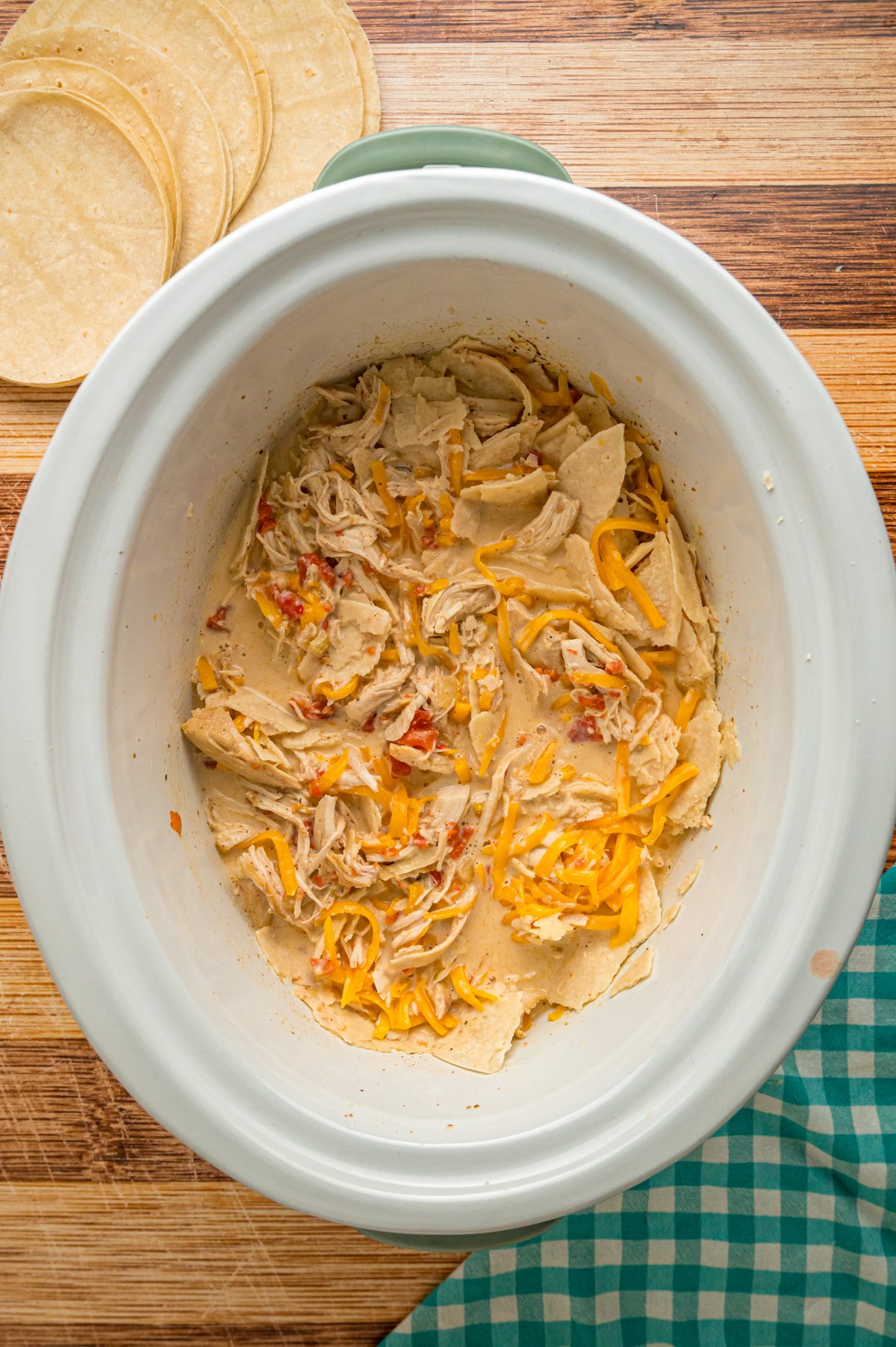 Cream mixture, tortillas, and cheese added to cooked chicken in a crockpot.