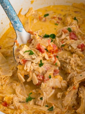 A metal spoon scooping chicken from a crockpot.