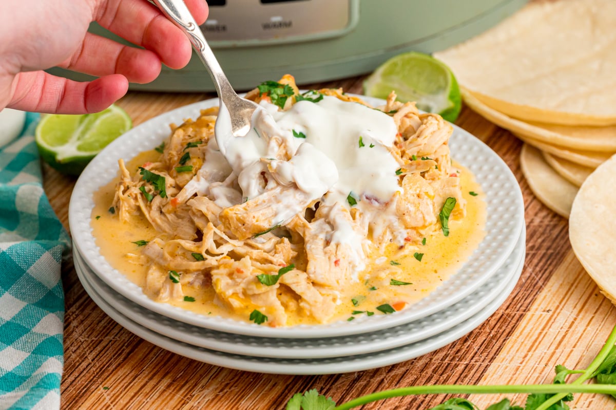 A hand holding a fork grabbing some chicken from to top of a stack of white plates.